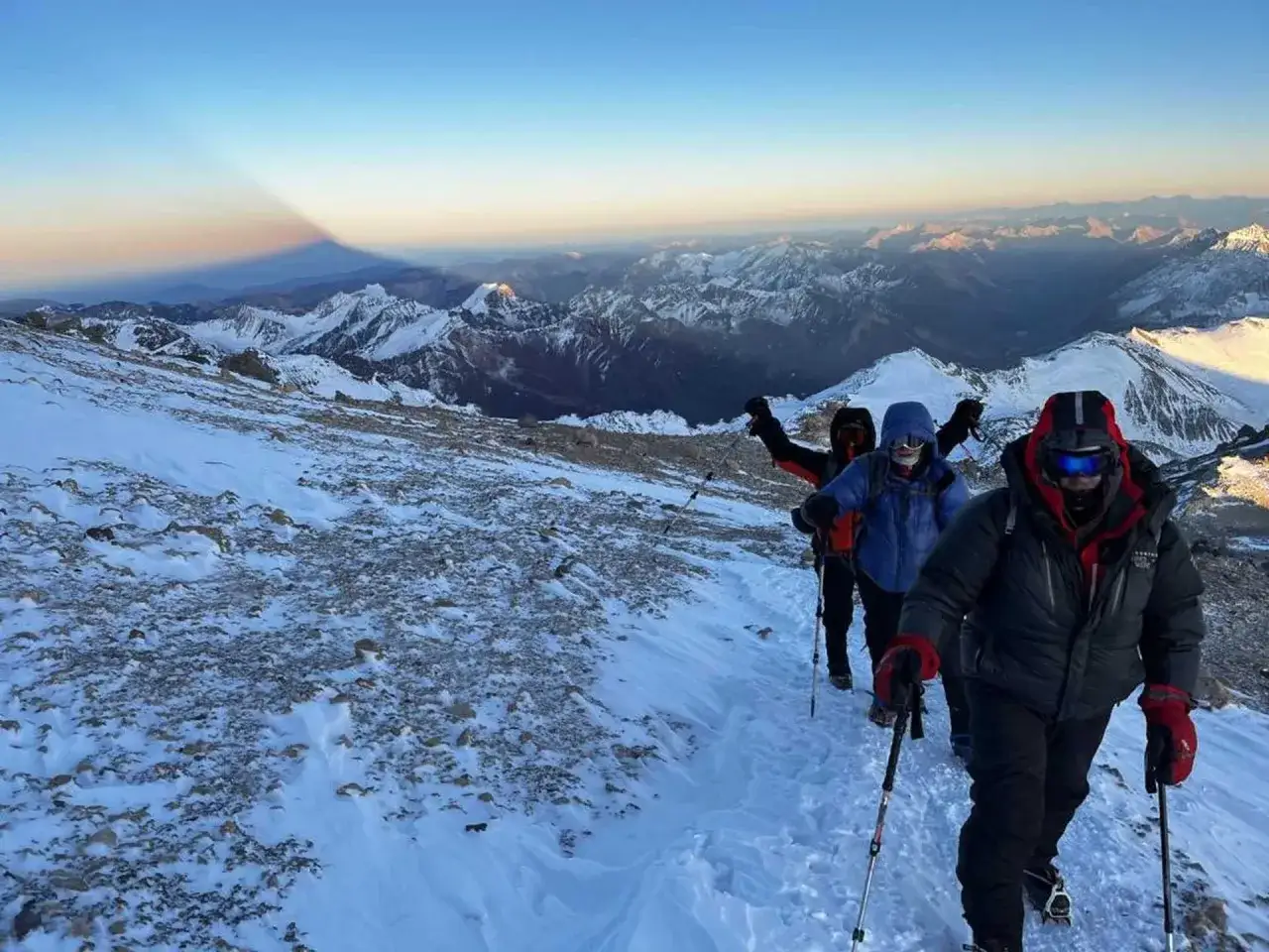 Wyprawa na Aconcaguę. Grupa alpinistów w ciepłej odzieży i z kijkami wspina się po ośnieżonym zboczu, podziwiając rozległy górski krajobraz i cień góry.
