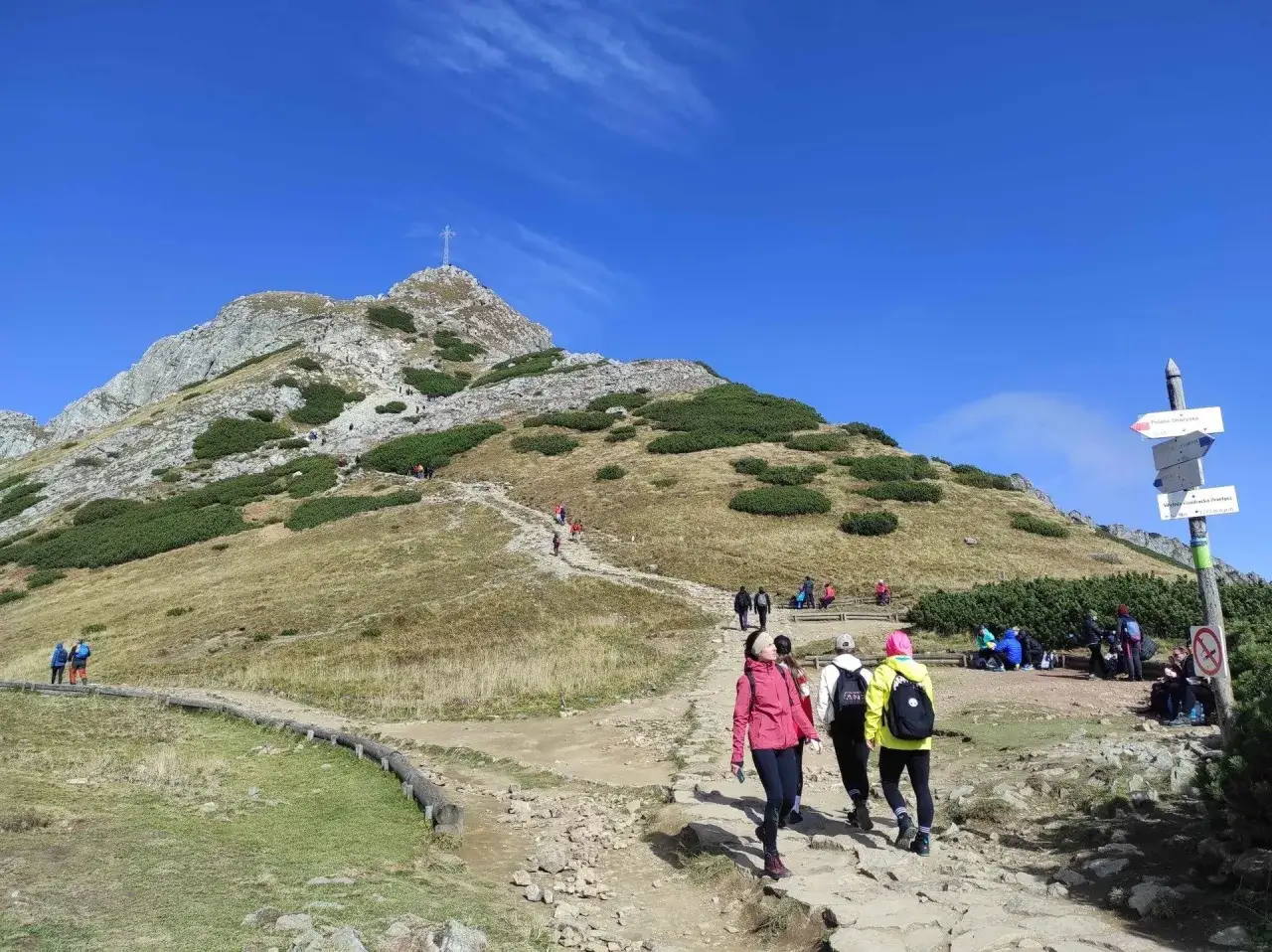 Ludzie idą szlakiem na Giewont. Czerwony szlak prowadzi pod górę, gdzie widać krzyż.