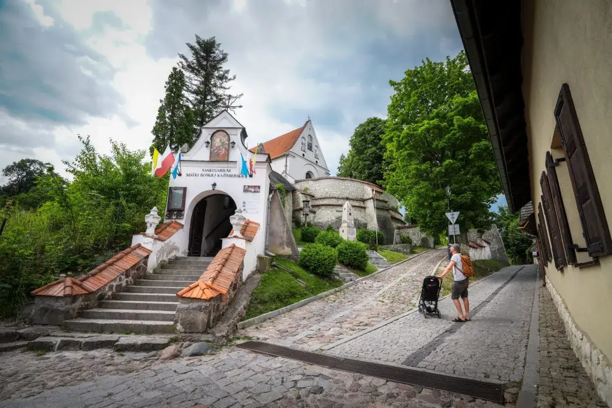 Sanktuarium w Kazimierzu Dolnym, idealne miejsce, gdzie na weekend lubelskie. Mężczyzna z wózkiem spaceruje brukowaną uliczką.