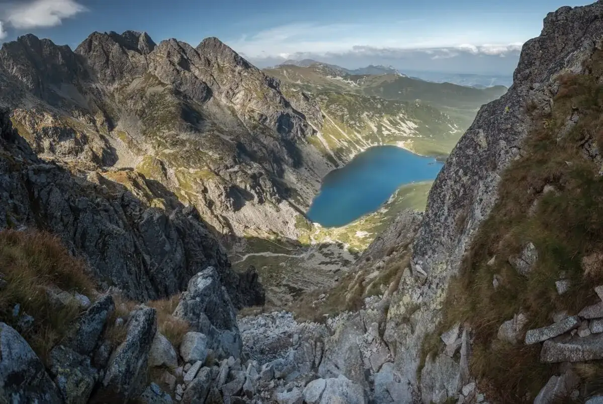 Widok z góry na skalisty szlak na granaty, prowadzący do turkusowego jeziora w dolinie.