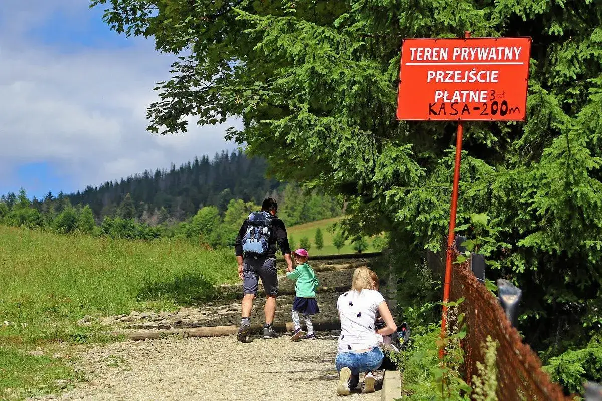 Rodzina wyrusza na zejście z Gubałówki. Tablica informuje o prywatnym, płatnym przejściu.