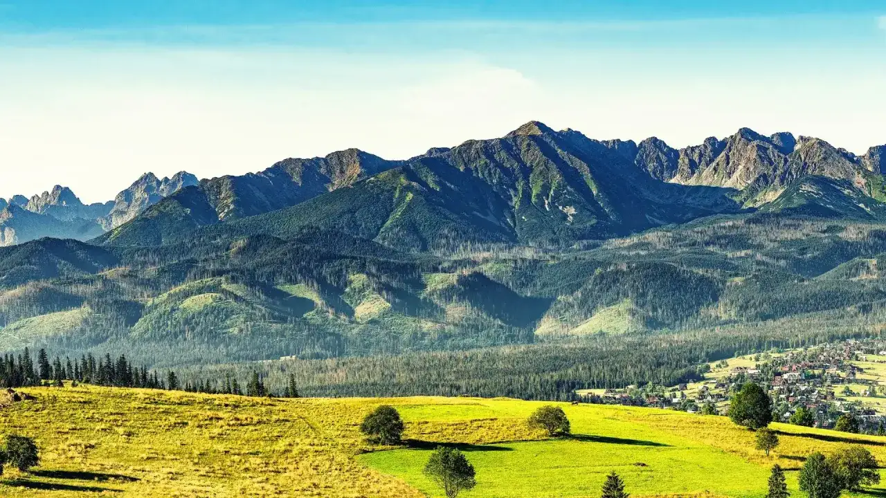 Majestatyczne Tatry w słońcu. Zielone łąki i lasy schodzą ku urokliwej wiosce. Ciekawe widoki z góry zapierają dech w piersiach.