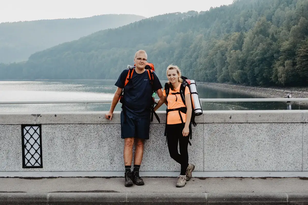 Para na moście, gotowa na mały szlak beskidzki. Plecaki spakowane, widok na jezioro i góry zachwyca.