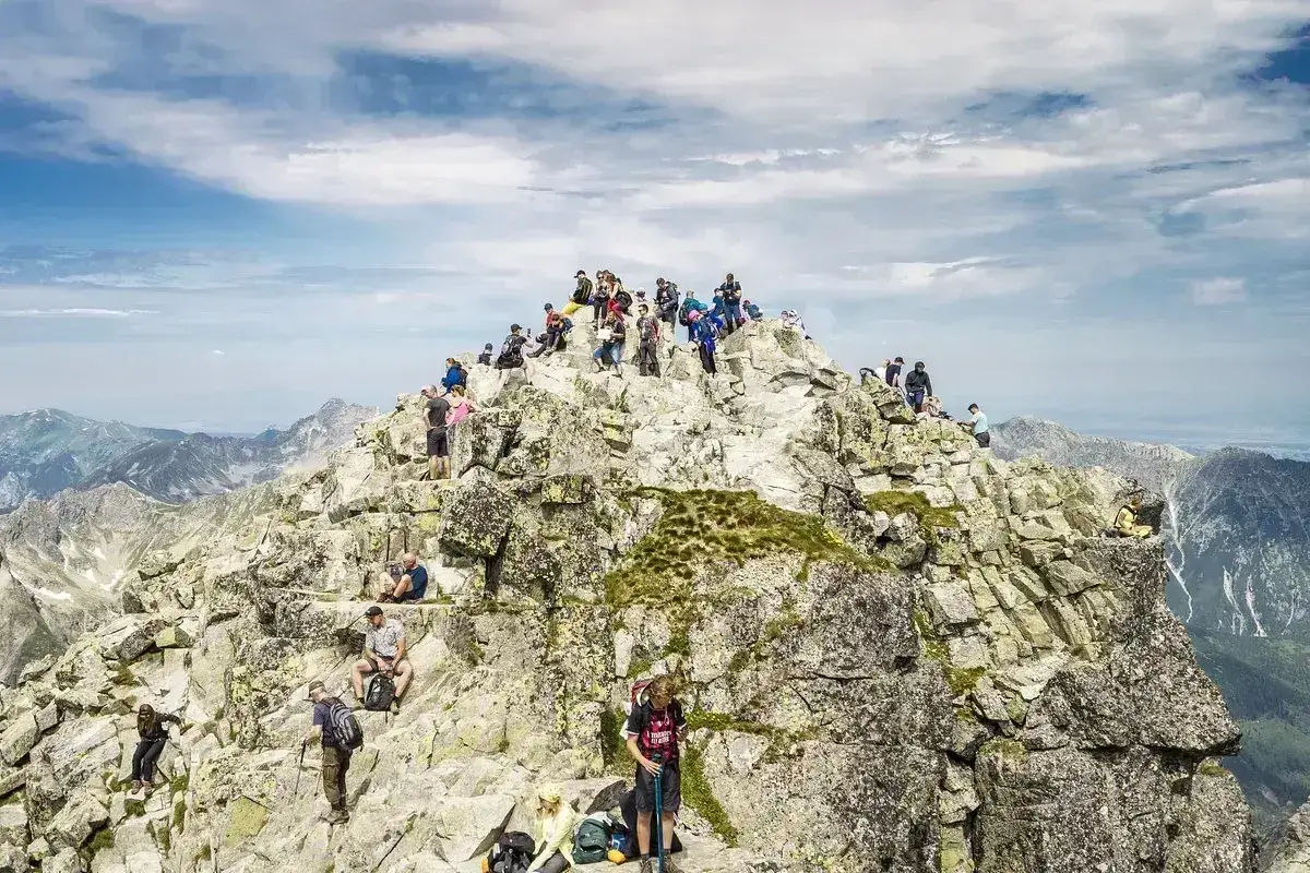 Tłum ludzi na skalistym szczycie Rysów. Wspinacze odpoczywają po trudach szlaku, podziwiając panoramę Tatr.