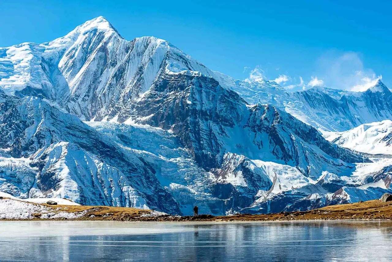 Majestatyczne góry podczas trekkingu Annapurna Circuit. Samotny turysta podziwia lodowce i zamarznięte jezioro.