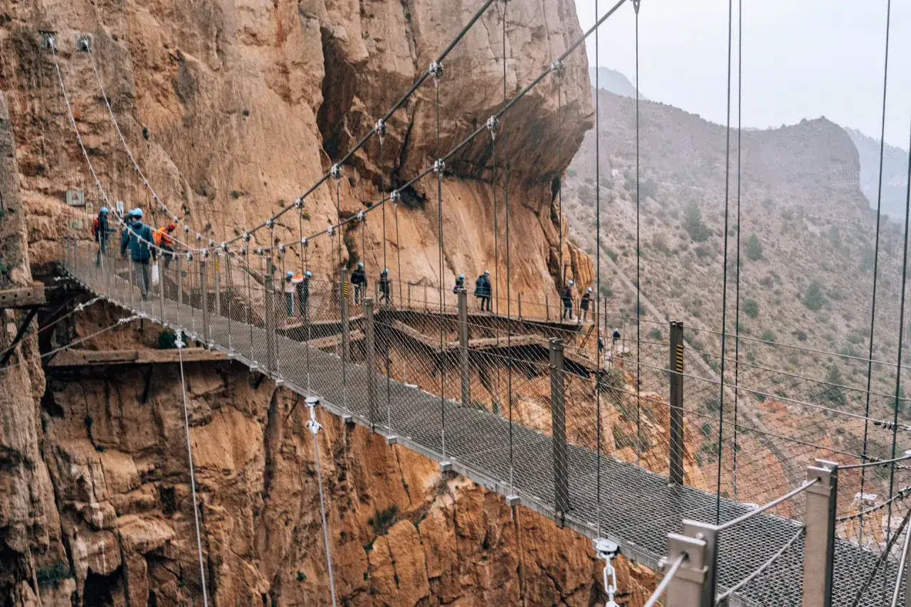 Ludzie spacerują po wiszącym moście Caminito del Rey, zawieszonym wysoko nad skalistym wąwozem.