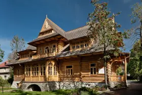 Drewniana willa "Antałówka" z bogatymi zdobieniami, kamienną podmurówką i drzewem jarzębiny z czerwonymi owocami.