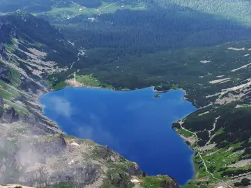 Górski staw gąsienicowy otoczony zielonymi zboczami i lasem iglastym.