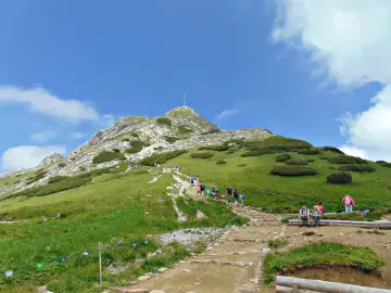 Tłum turystów wspina się kamienistym szlakiem na Giewont. Widać krzyż na szczycie.
