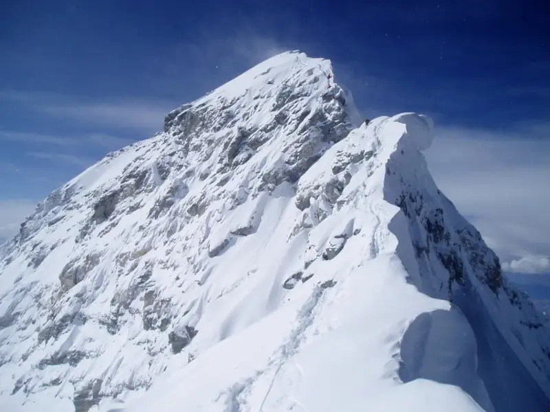 Ośnieżony, skalisty szczyt Mount Everest, z kilkoma wspinaczami na grani. Widać ślady na śniegu, jak wygląda szczyt Mount Everest.